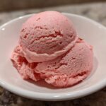 Two scoops of vibrant pink strawberry ice cream served in a small white bowl.