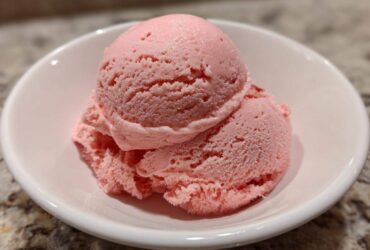 Two scoops of vibrant pink strawberry ice cream served in a small white bowl.