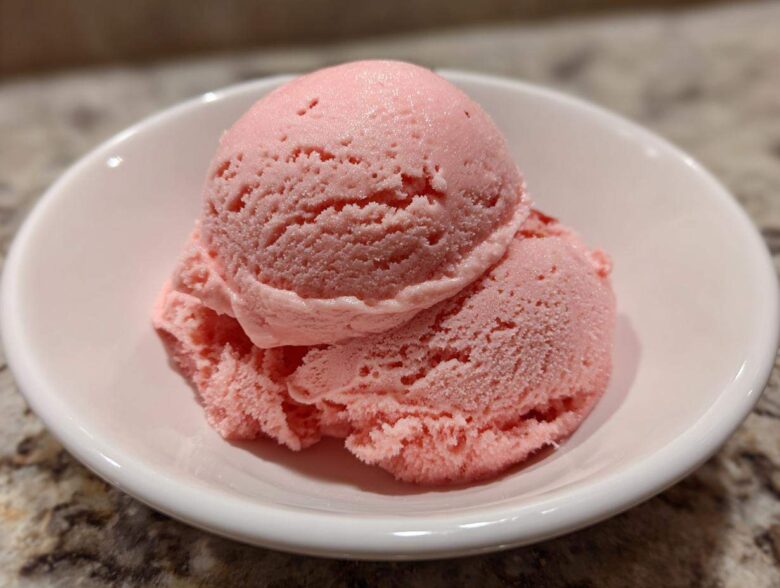 Two scoops of vibrant pink strawberry ice cream served in a small white bowl.