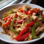 Close-up of shredded chicken mixed with sliced red and green bell peppers and onions for crockpot chicken fajitas.