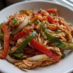 Close-up of shredded chicken mixed with colorful bell peppers and onions, ready for crockpot chicken fajitas.