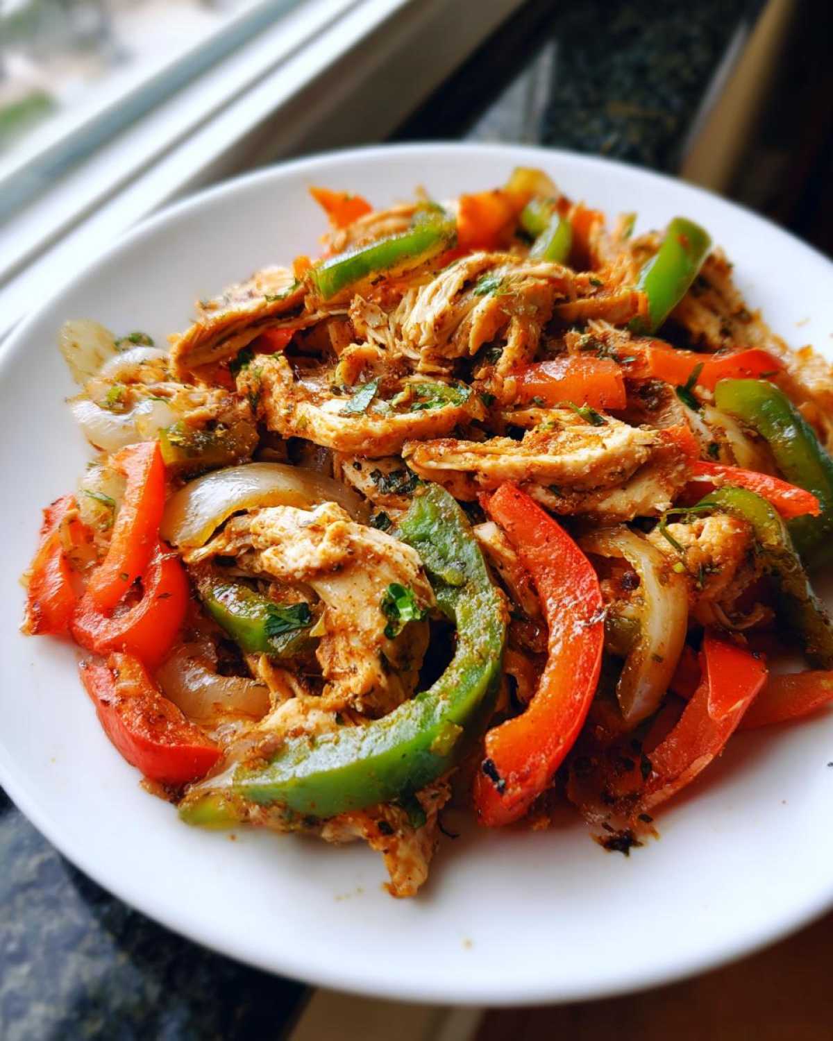 Close-up of shredded chicken mixed with sautéed red and green bell peppers and onions for crockpot chicken fajitas.
