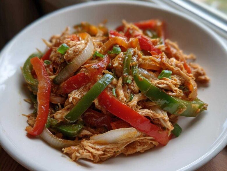 Close-up of shredded chicken mixed with colorful bell peppers and onions, ready for crockpot chicken fajitas.