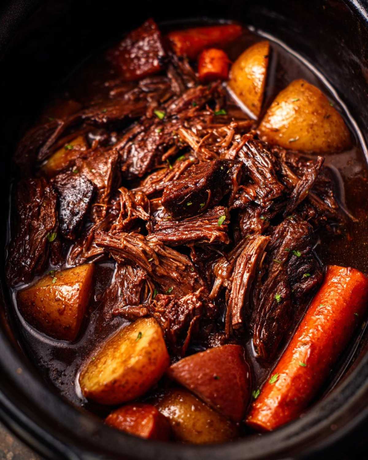 Close-up of tender, shredded pot roast cooked with large chunks of carrots and potatoes in a rich brown sauce.