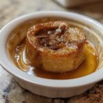 A single serving of a baked apple, caramelized and sitting in sweet brown syrup in a white ramekin.