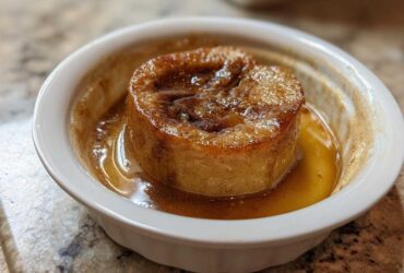 A single serving of a baked apple, caramelized and sitting in sweet brown syrup in a white ramekin.