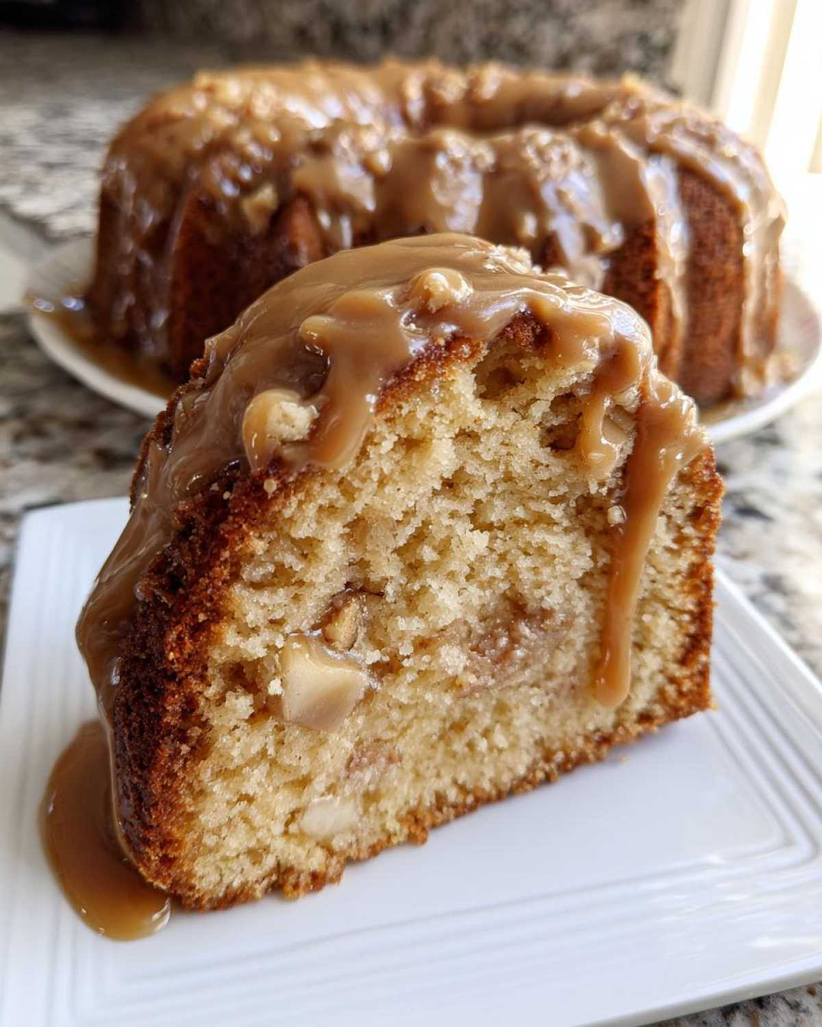 Close-up of a slice of moist apple bundt cake topped with thick caramel glaze.