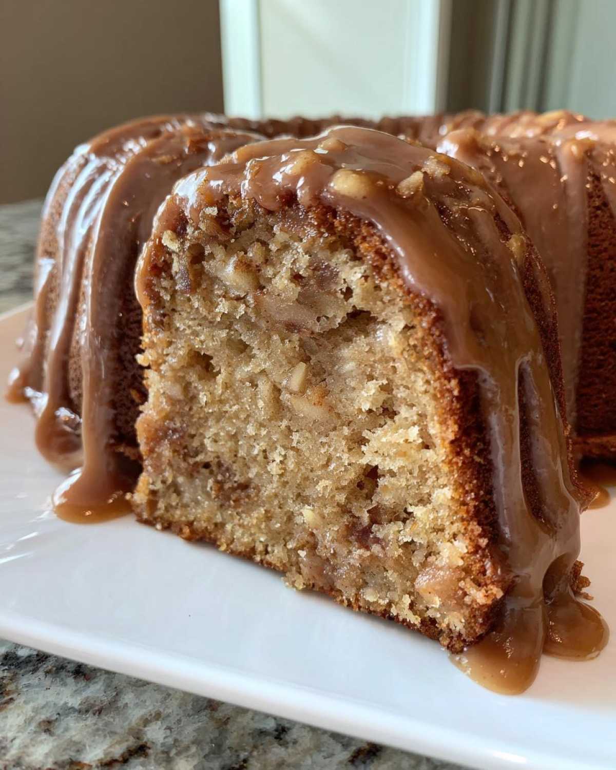 Close-up of a slice of moist apple bundt cake topped with thick, dripping caramel glaze.