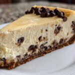 A perfect slice of creamy chocolate chip cheesecake with a graham cracker crust and chocolate chips on top.