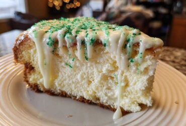 A close-up of a slice of creamy christmas tree cheesecake topped with white icing drizzle and green sprinkles.