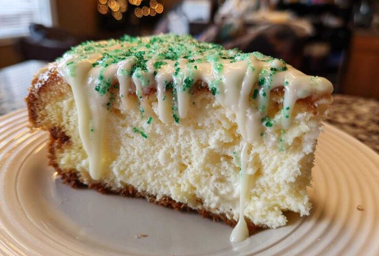 A close-up of a slice of creamy christmas tree cheesecake topped with white icing drizzle and green sprinkles.