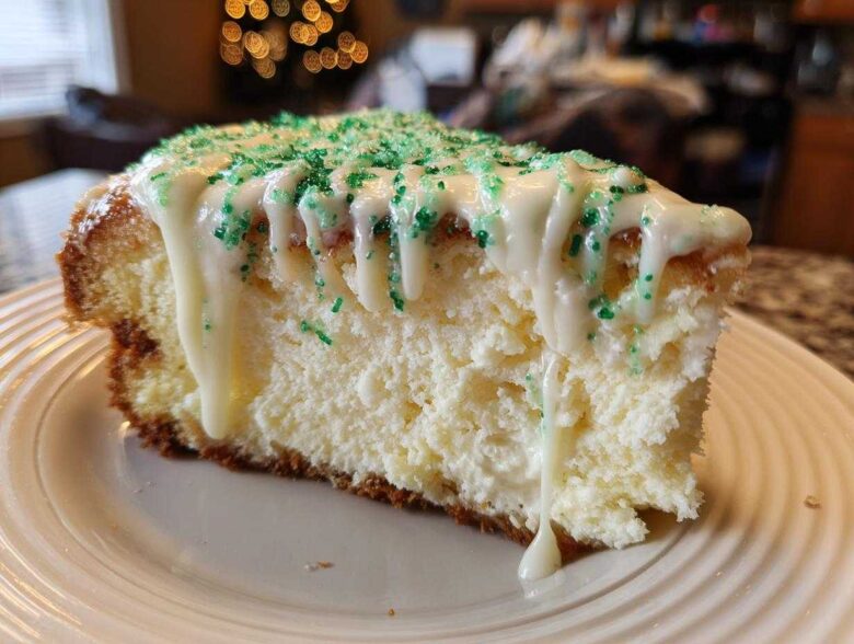 A close-up of a slice of creamy christmas tree cheesecake topped with white icing drizzle and green sprinkles.