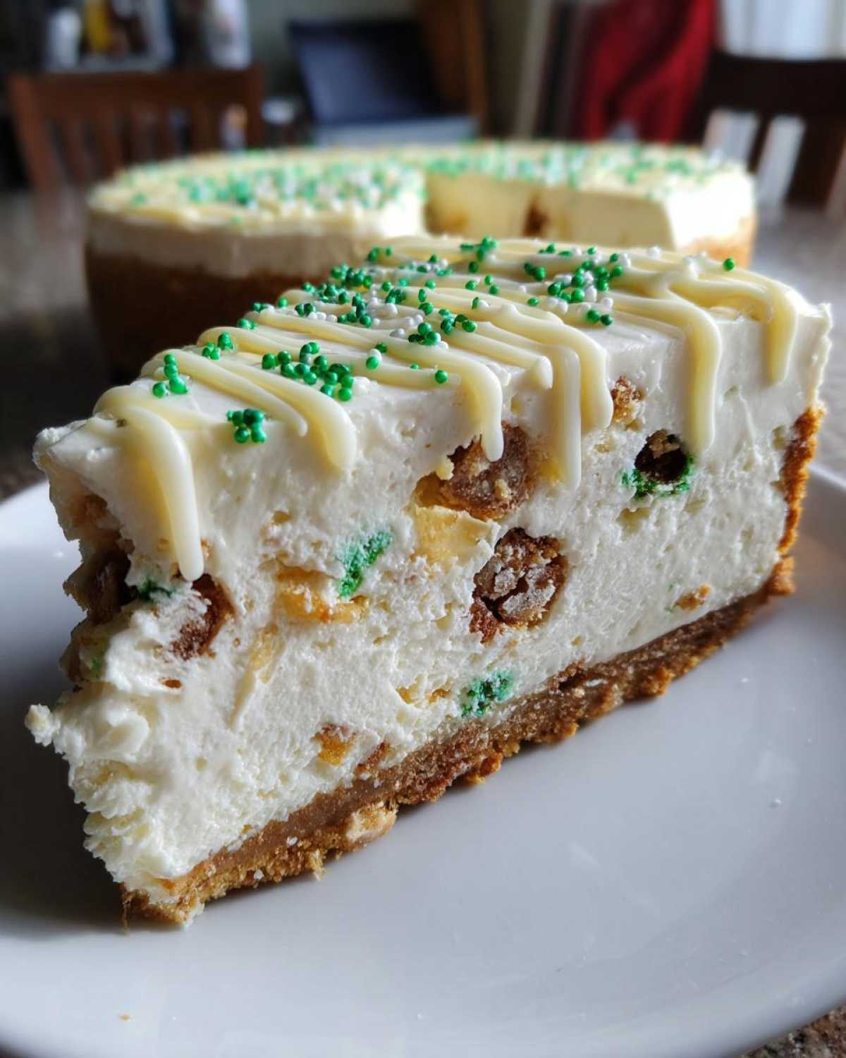 Close-up of a slice of christmas tree cheesecake topped with white chocolate drizzle and green sprinkles.