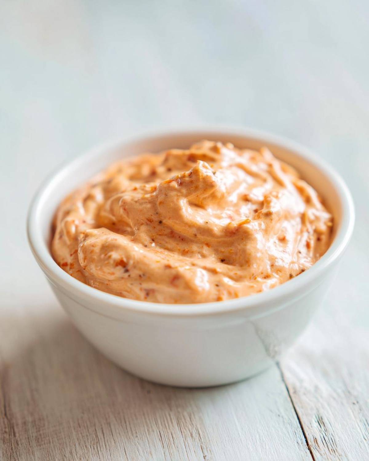 Close-up of creamy, orange-hued smash burger sauce swirled in a small white bowl.