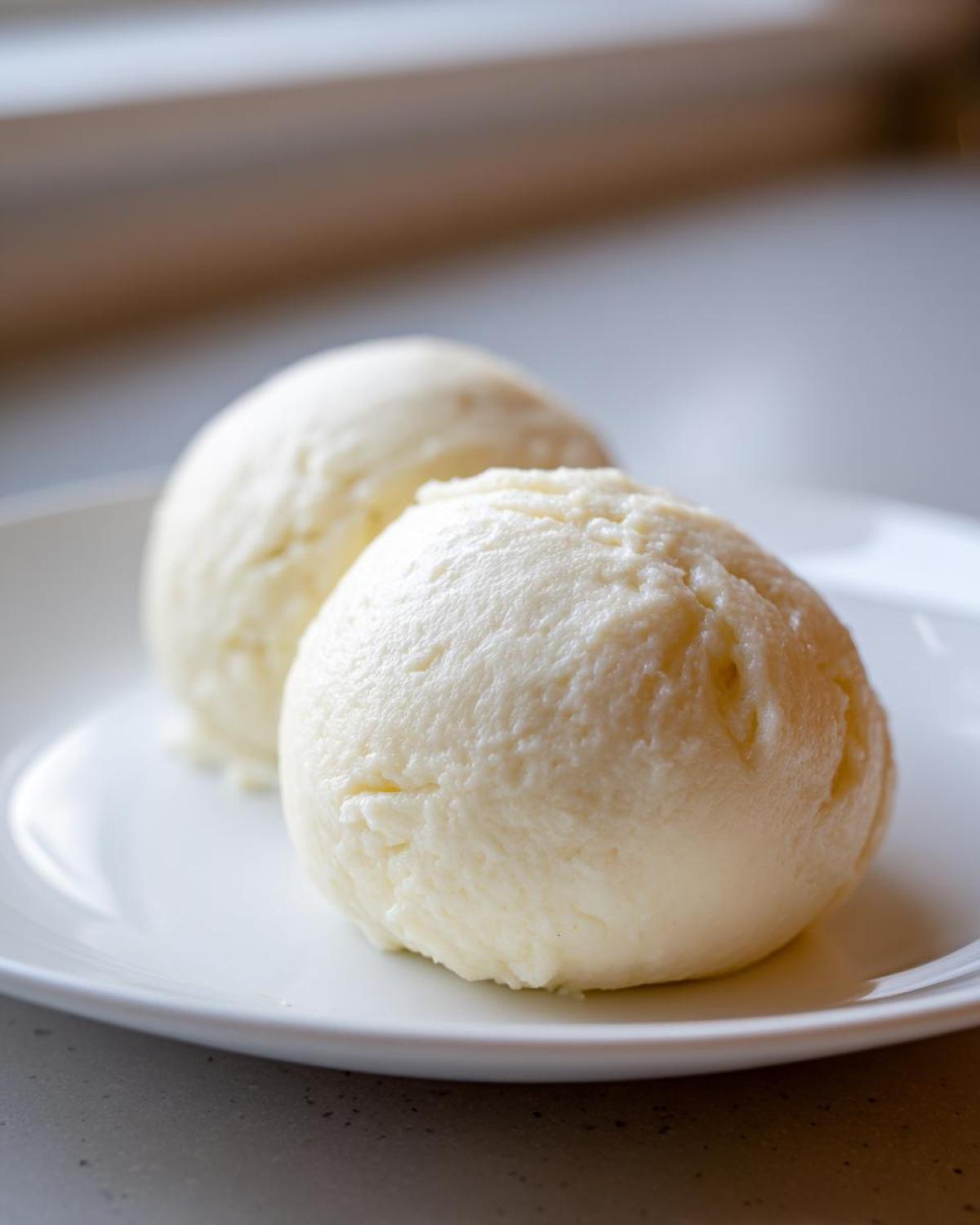 Two smooth, pale yellow balls of freshly made fufu served on a white plate, ready to eat.