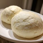 Two perfectly shaped, smooth balls of homemade fufu resting on a white serving plate.