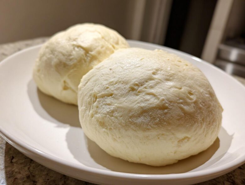 Two perfectly shaped, smooth balls of homemade fufu resting on a white serving plate.