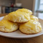 A stack of soft, round ricotta cookies topped with bright yellow lemon glaze and zest.