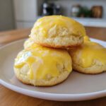 A close-up of soft, thick ricotta cookies topped with a bright yellow lemon glaze and zest.