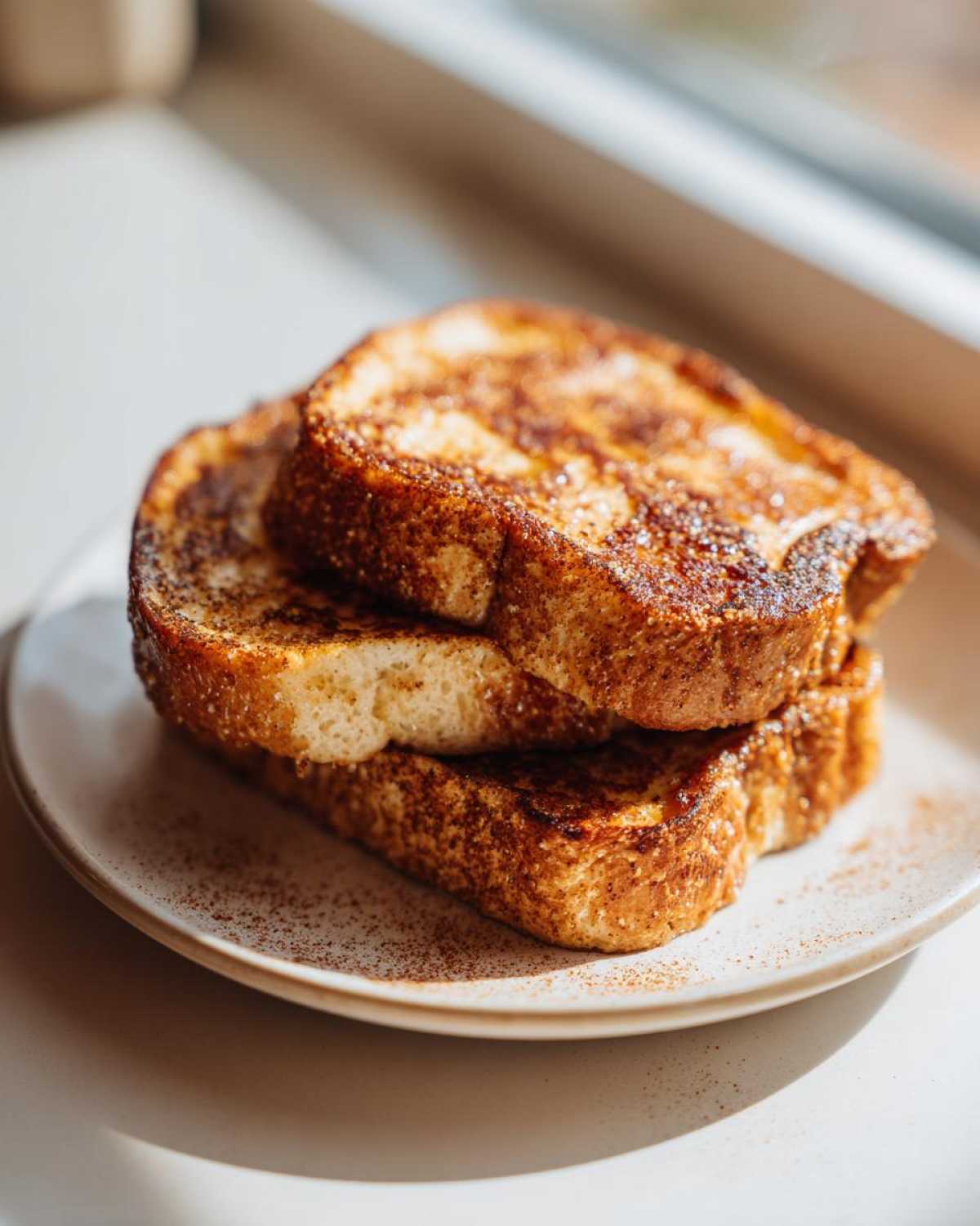 A stack of three slices of golden brown sourdough french toast dusted heavily with cinnamon.