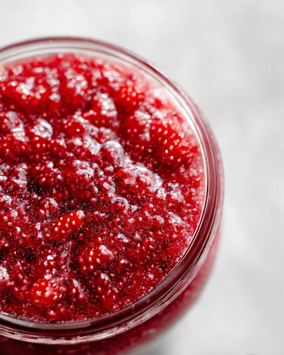 Close-up overhead view of vibrant red strawberry freezer jam filled to the brim in a glass jar.