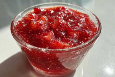 Close-up of vibrant red strawberry freezer jam with visible seeds, served in a small clear glass bowl.