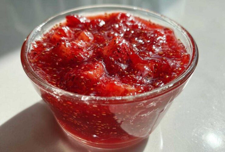 Close-up of vibrant red strawberry freezer jam with visible seeds, served in a small clear glass bowl.
