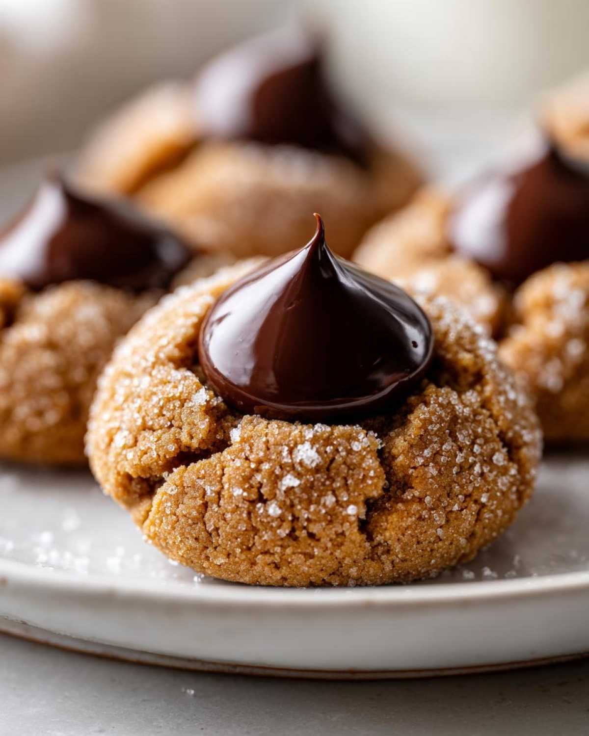 A close-up of a freshly baked, sugar-coated kiss cookie topped with a glossy dollop of melted chocolate.