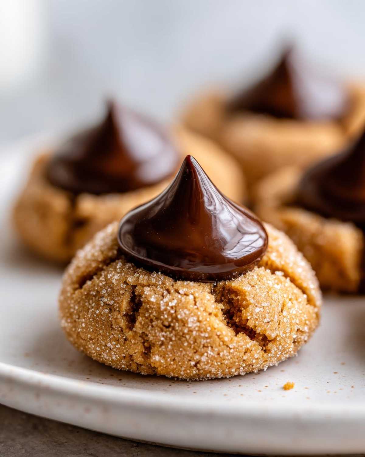 A close-up of a freshly baked, sugar-coated peanut butter kiss cookie topped with a melted chocolate kiss.