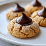 A close-up of a perfectly baked, sugar-coated peanut butter kiss cookie topped with a glossy chocolate Hershey's Kiss.