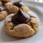 A close-up shot of a perfectly baked peanut butter kiss cookie, rolled in sugar and topped with a melted chocolate kiss.