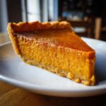 A close-up, appetizing slice of rich orange sweet potato pie resting on a white plate.