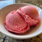 Close-up of two scoops of vibrant pink strawberry ice cream served in a small white bowl.