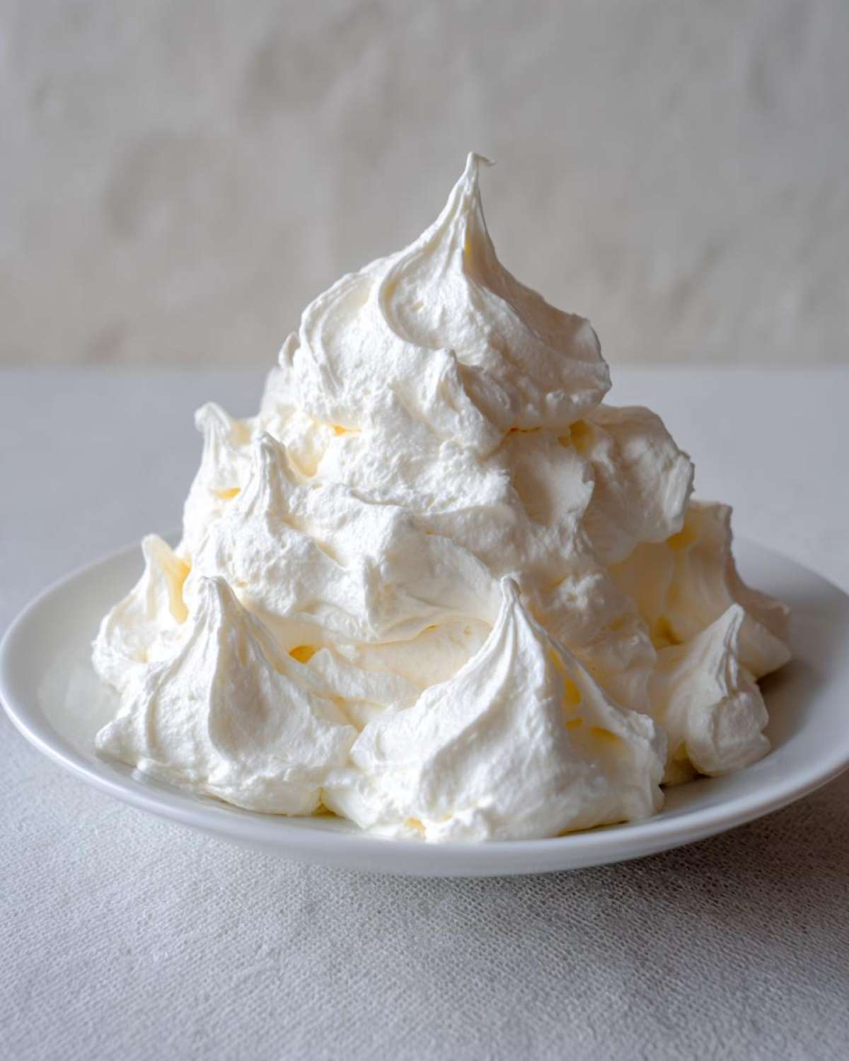 A large, perfectly piped mound of bright white vanilla buttercream frosting sitting on a white plate.