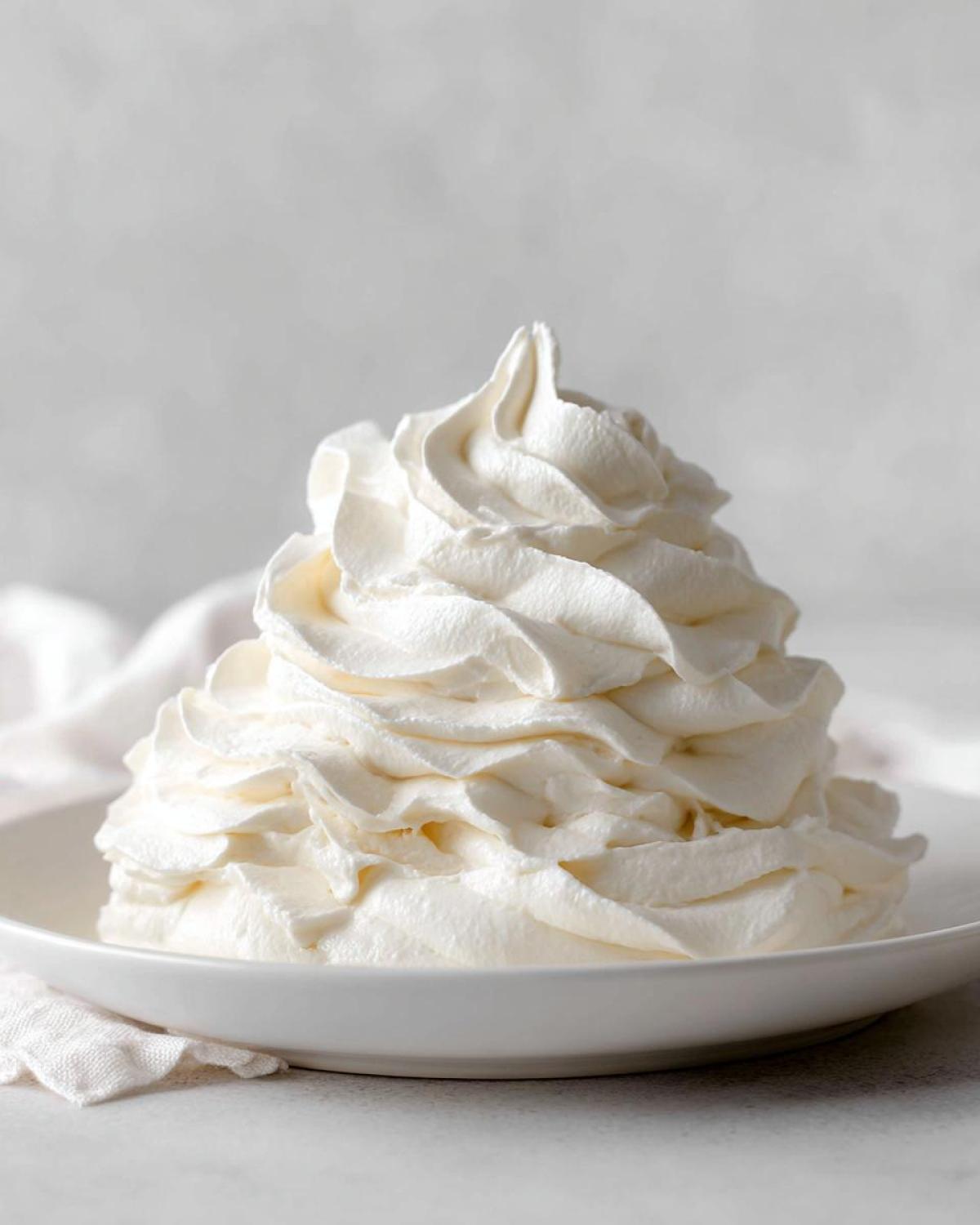 A tall, beautifully piped mound of creamy white vanilla buttercream frosting in a white bowl.