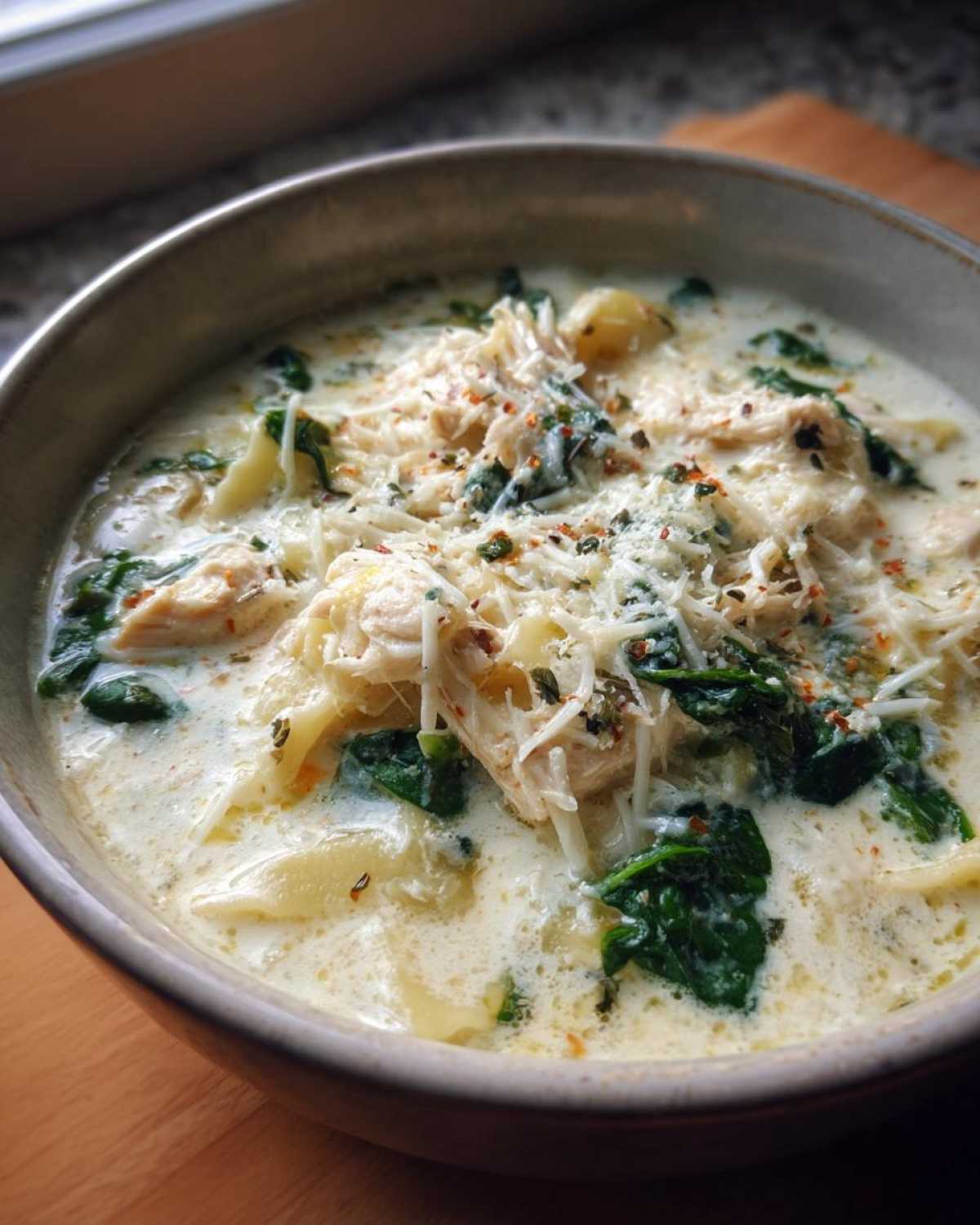 Close-up of a bowl of rich white chicken lasagna soup topped with shredded chicken, spinach, and Parmesan cheese.