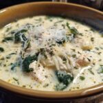 Close-up of a rich white chicken lasagna soup garnished with spinach, shredded cheese, and herbs.