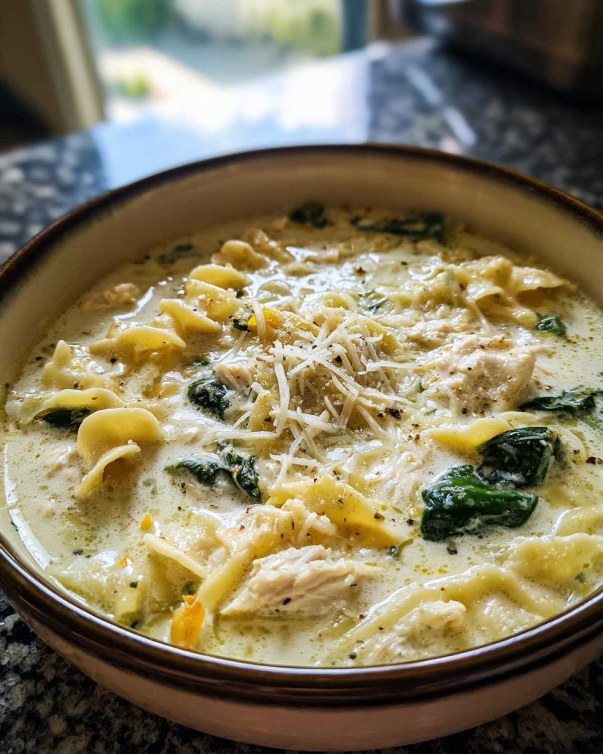 Close-up of a bowl of creamy white chicken lasagna soup topped with shredded Parmesan cheese.