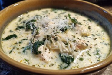 Close-up of a rich white chicken lasagna soup garnished with spinach, shredded cheese, and herbs.