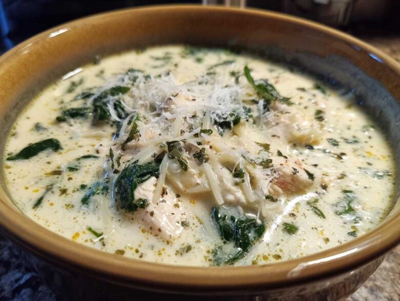Close-up of a rich white chicken lasagna soup garnished with spinach, shredded cheese, and herbs.