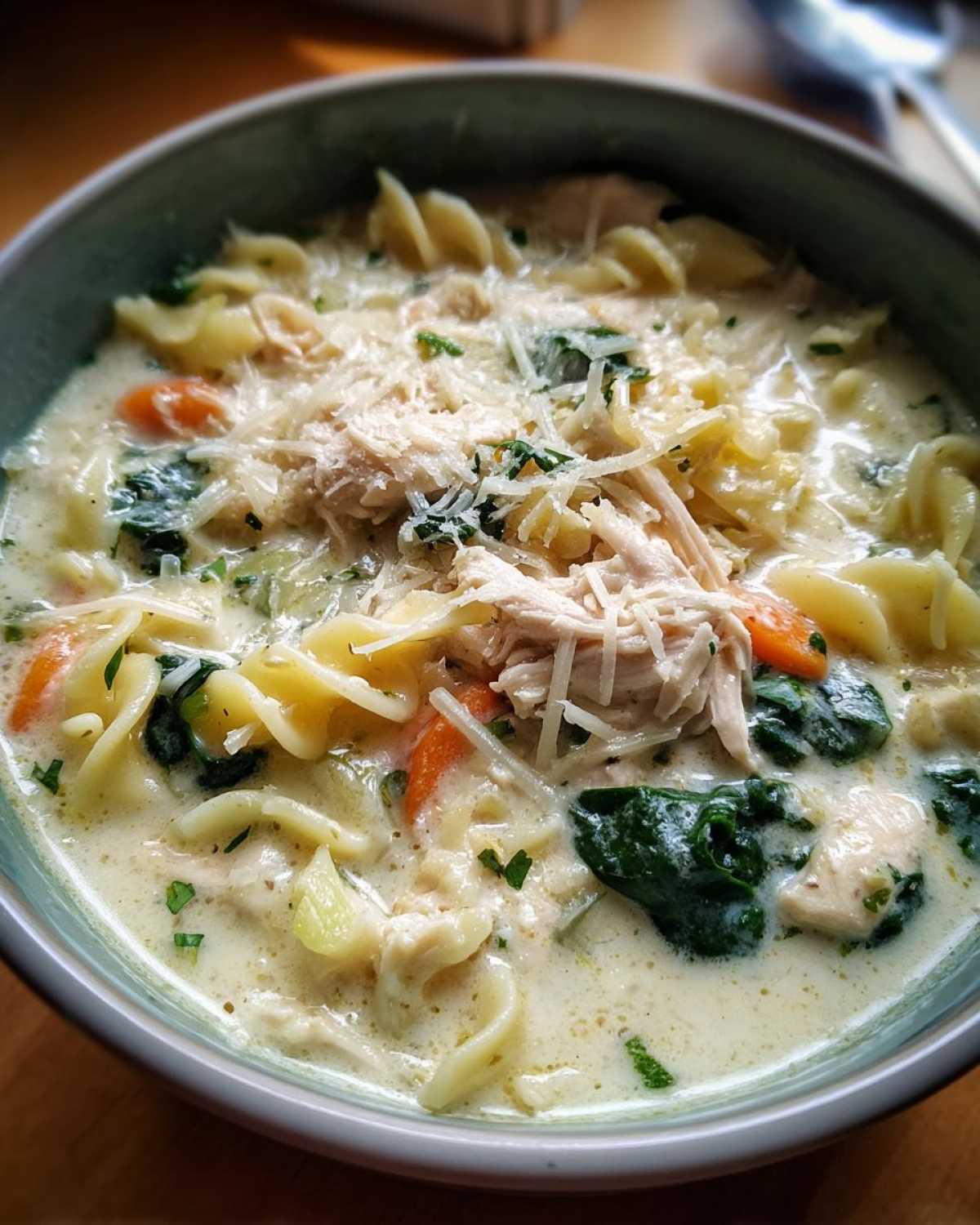 Close-up of a bowl of rich white chicken lasagna soup topped with shredded chicken, spinach, and Parmesan cheese.