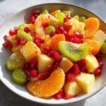Close-up of a colorful winter fruit salad featuring oranges, kiwi, grapes, and pomegranate seeds.
