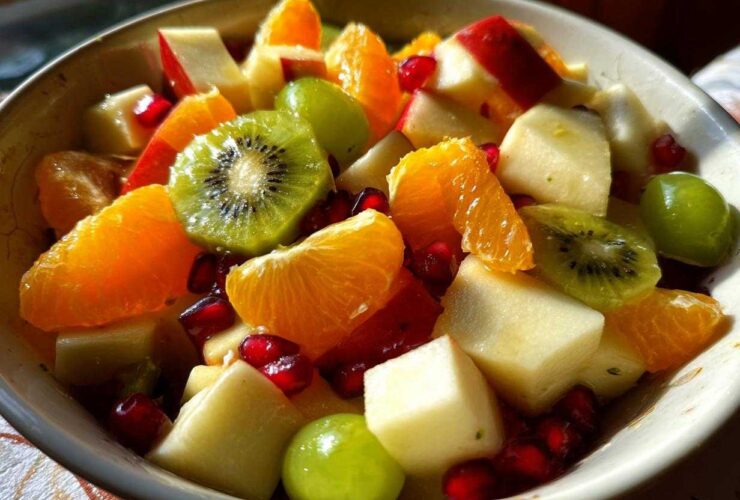 Close-up of a vibrant winter fruit salad featuring kiwi slices, orange segments, apple chunks, grapes, and pomegranate seeds.