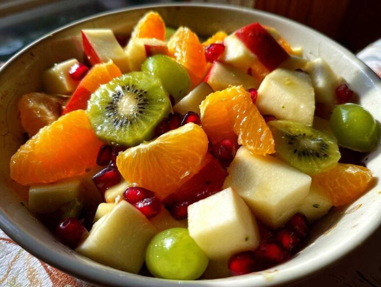 Close-up of a vibrant winter fruit salad featuring kiwi slices, orange segments, apple chunks, grapes, and pomegranate seeds.
