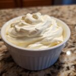 A close-up of creamy, whipped horseradish sauce mounded high in a small white bowl on a granite countertop.