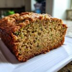A close-up of a freshly baked slice of zucchini banana bread showing the moist crumb and flecks of green zucchini.
