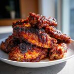 A close-up stack of crispy, glazed Air Fryer BBQ Chicken Wings piled high on a white plate.