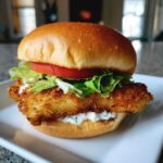 A perfectly assembled Air Fryer Crispy Fish Sandwich featuring a golden, breaded fillet, lettuce, tomato, and tartar sauce.