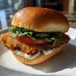 Close-up of an Air Fryer Crispy Fish Sandwich featuring a golden breaded fillet, lettuce, tomato, and tartar sauce on a brioche bun.