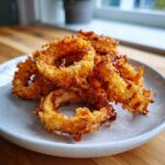 A pile of golden brown, crispy Air Fryer Onion Rings served on a light gray plate.